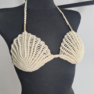Può includere: Un top bikini in crochet color crema con un design a conchiglia e dettagli dorati.