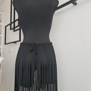 Close-up of the back view of a black macramé skirt, showcasing intricate patterns and detailed craftsmanship, with a focus on the ties and design.