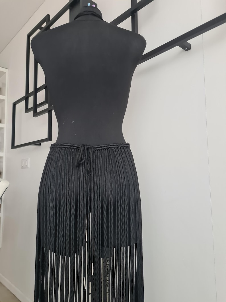 Close-up of the back view of a black macramé skirt, showcasing intricate patterns and detailed craftsmanship, with a focus on the ties and design.