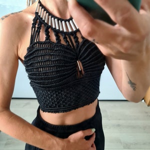 A model in front of a mirror, showcasing a black macramé top with metallic details. The intricate design and metallic accents are highlighted, emphasizing the bohemian elegance and craftsmanship of the top.