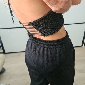 A model in front of a mirror, showcasing the back of a macramé top with a tied knot design. The focus is on the detailed knotting and the elegant bohemian style of the top.