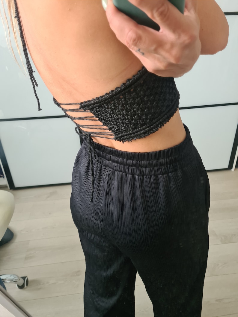 A model in front of a mirror, showcasing the back of a macramé top with a tied knot design. The focus is on the detailed knotting and the elegant bohemian style of the top.