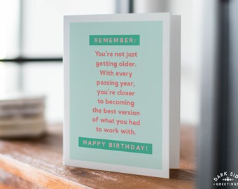 May include: A folded birthday card with a light teal background and white border. The card reads "REMEMBER: You're not just getting older...HAPPY BIRTHDAY!" in white and teal text. The Dark Side Greetings logo is in the bottom right corner.