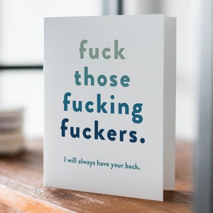 May include: A white greeting card with the text "fuck those fucking fuckers." in shades of green and blue. The card also includes the phrase "I will always have your back." The Dark Side Greetings logo is in the bottom right corner.