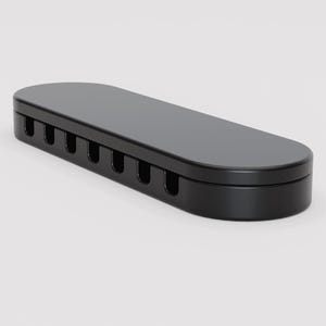 May include: A black cable organizer with a rounded rectangular shape. The top surface is smooth, while the side has several evenly spaced slots. The organizer is designed to hold and manage cables, keeping them neat and organized.