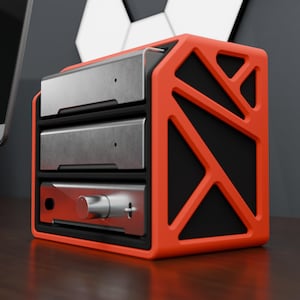 May include: A bright orange, geometric, open-frame storage rack holding three stacked silver electronic components. The bottom unit features a prominent circular control knob on its front face, while the top two units have smooth, solid silver panels.