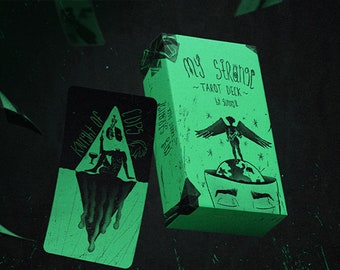 May include: A green box with the text "My Strange Tarot Deck" and an illustration of a winged figure standing on a globe. The box is next to a tarot card with the text "Knight of Cups" and an illustration of a figure holding a cup.