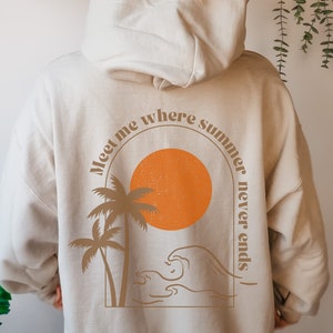 May include: A beige hoodie with a graphic print on the back. The graphic features a sun, palm trees, waves, and the text "Meet me where summer never ends".