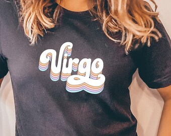 Może przedstawiać: Ciemnoszara koszulka z napisem "Virgo" w stylu retro, warstwową czcionką. Koszulka jest połączona z legginsami w panterkę. Słowo "Virgo" jest białe z pastelowymi akcentami kolorystycznymi.