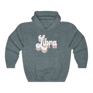 K&ouml;nnte beinhalten: Ein dunkelblauer Kapuzenpullover mit einer wei&szlig;en Retro-Grafik, auf der "Libra" in Regenbogenfarben steht.