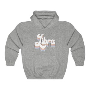 K&ouml;nnte beinhalten: Ein grauer Kapuzenpullover mit dem Wort "Libra" in einer retro-Regenbogen-Schrift auf der Vorderseite.