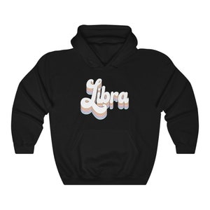 K&ouml;nnte beinhalten: Schwarzer Kapuzenpullover mit einem wei&szlig;en Retro-&bdquo;Libra&ldquo;-Motiv in Regenbogenfarben.