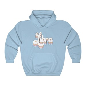 K&ouml;nnte beinhalten: Hellblauer Kapuzenpullover mit dem Wort "Libra" in einer Retro-Schriftart in Regenbogenfarben.