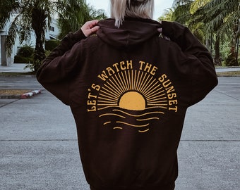 May include: A black hoodie with a yellow graphic on the back that says "Let's watch the sunset" with a stylized sun and waves.