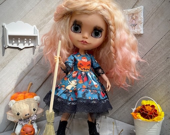 Puede incluir: Una muñeca con cabello rosado y un vestido azul con un diseño de calabaza de Halloween, sosteniendo una escoba. La muñeca lleva botas negras y está rodeada de calabazas, hojas de otoño y un oso de peluche con cabeza de calabaza.