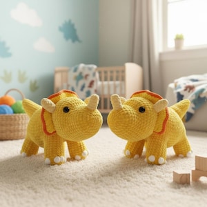 May include: Two yellow crocheted triceratops toys with orange and white accents. The dinosaur toys have black eyes and stand on a light-colored carpet. The background includes a crib, a basket of colorful balls, and a window.