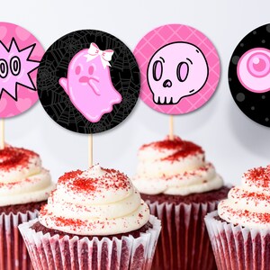 Könnte beinhalten: Vier Cupcakes mit pinkfarbenen und schwarzen Halloween-Cupcake-Toppern. Die Topper zeigen einen Geist, einen Schädel, Augen und eine Sprechblase mit dem Wort "BOO".