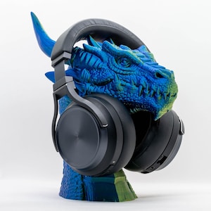 May include: A blue and green dragon head sculpture with black headphones. The dragon has detailed scales and horns. The headphones are over-ear style, with large, round earcups. The sculpture is a headphone stand.