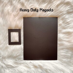 Puede incluir: Dos imanes rectangulares negros sobre una superficie blanca y esponjosa. El texto "Heavy Duty Magnets" est&aacute; por encima de los imanes.