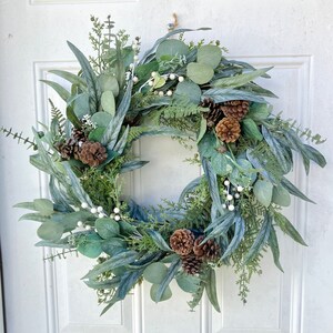 Op de afbeelding: Een groene en witte eucalyptuskrans met bruine dennenappels en witte bessen.