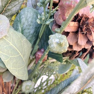 Op de afbeelding: Een close-up van een kunstbloemenarrangement met dennenappels, eucalyptusbladeren en ander groen. De opstelling is perfect om elke ruimte een vleugje natuur te geven.