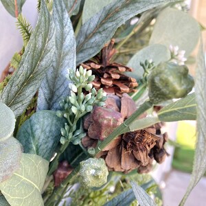 Op de afbeelding: Close-up van een groene eucalyptuskrans met bruine dennenappels en kleine groene bessen.
