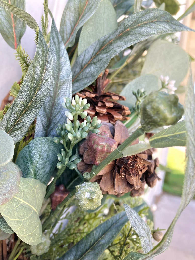 Op de afbeelding: Close-up van een groene eucalyptuskrans met bruine dennenappels en kleine groene bessen.