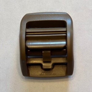 May include: A brown plastic buckle with a rectangular shape and a smooth surface. The buckle has a small, rectangular opening in the center.