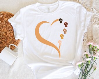 May include: White t-shirt with a brown heart shape and five raised fists of different skin tones.