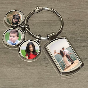May include: Silver metal keyring with a rectangular photo pendant and three circular photo pendants. The photos show a dog, a young boy, a young girl, and a couple. The keyring is on a wooden surface.