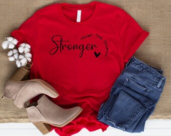 May include: Red t-shirt with the text "Stronger Than The Storm" in black lettering with a small heart symbol.