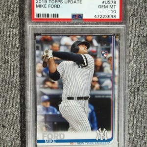 May include: A 2019 Topps Update baseball card featuring Mike Ford of the New York Yankees. The card is graded GEM MT 10 and encased in a protective holder. The card shows Ford in a batting stance.