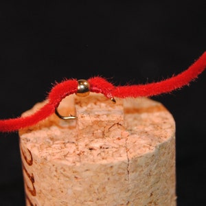 May include: A red fuzzy worm fly fishing lure with a gold bead.