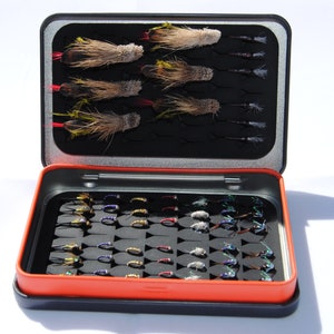 May include: An open black fly fishing box with a red interior. The box is filled with a variety of colourful flies.