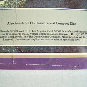 May include: Close-up of a vintage record album cover with text. The text reads "Also Available On Cassette and Compact Disc." Below, the text includes the record label's address and copyright information. The background has a faded, textured appearance.