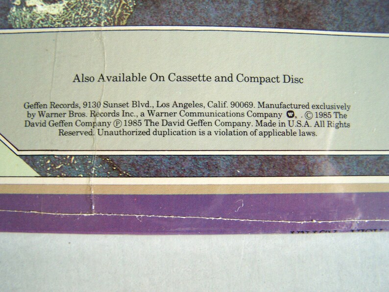 May include: Close-up of a vintage record album cover with text. The text reads "Also Available On Cassette and Compact Disc." Below, the text includes the record label's address and copyright information. The background has a faded, textured appearance.