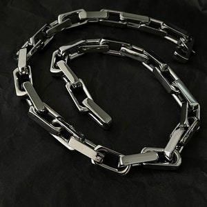 Peut inclure: Un collier en chaîne argent avec un design de maillon carré. La chaîne est en métal et a une finition polie.