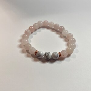 May include: A bracelet made with light pink and white beads. The bracelet has two larger white beads with copper accents.