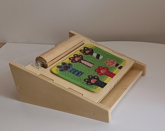 May include: A wooden ramp with a rolling cylinder at the top and a colorful paw print puzzle piece at the bottom. The ramp is made of light wood and has a natural finish. The puzzle piece is made of fabric and has a green background with colorful paw prints.