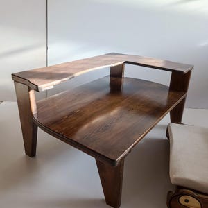 May include: A dark brown wooden table with a two-tiered design featuring a lower rectangular surface and an elevated, narrower upper shelf supported by vertical wooden legs. The wood grain is visible throughout the polished finish.