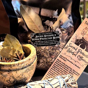 Puede incluir: Un surtido de productos herbales para prácticas espirituales. Incluye una bolsa de hierbas, un mortero y una maja llenos de hierbas, un manojo de salvia atado con hilo azul y una tarjeta con texto.