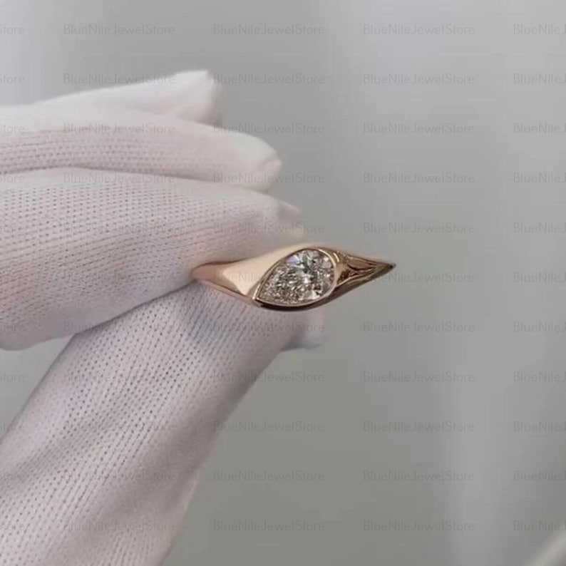 Puede incluir: Un anillo de oro rosa con un diamante central en forma de pera. El anillo tiene una banda lisa que se ensancha para sostener el diamante. El diamante est&aacute; engastado en un bisel. El dise&ntilde;o del anillo es elegante y moderno.
