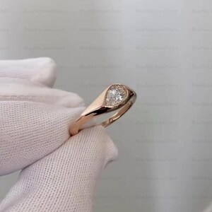 Puede incluir: Un anillo de oro rosa con un diamante en forma de pera. El diamante est&aacute; engastado en un bisel, y la banda tiene un acabado liso y pulido. El anillo es una joya cl&aacute;sica y elegante.