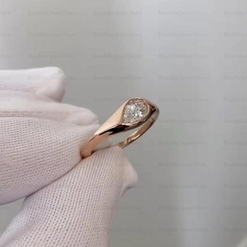 Puede incluir: Un anillo de oro rosa con un diamante en forma de pera. El diamante est&aacute; engastado en un bisel, y la banda tiene un acabado liso y pulido. El anillo es una joya cl&aacute;sica y elegante.
