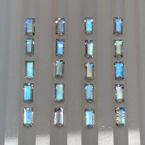 May include: Twenty-four iridescent rectangular gemstones arranged in four rows of six. The gemstones are a light blue color with a rainbow sheen.