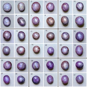 May include: A collection of 37 cabochon gemstones, each with a polished, rounded shape. The stones display a range of colors, including shades of purple, pink, and brown, with some exhibiting star-like patterns. The gemstones are arranged in a grid.