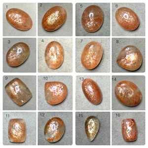 Puede incluir: Una colección de dieciséis cabujones de piedra solar pulidos, cada uno con tonos únicos de naranja, melocotón y dorado con inclusiones metálicas brillantes internas. Las piedras se muestran en una cuadrícula, exhibiendo varias formas ovaladas, rectangulares y de lágrima.