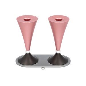 Könnte beinhalten: Ein Paar rosafarbene Metall-Menoras mit schwarzen Sockeln und einer silbernen Grundplatte. Die Menoras sind kegelförmig und haben ein modernes Design.