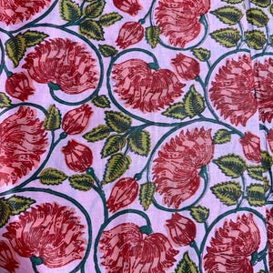 K&ouml;nnte beinhalten: Ein Stoff mit einem sich wiederholenden Blumenmuster. Gro&szlig;e rote Bl&uuml;ten und Knospen vor einem hellrosa Hintergrund, mit gr&uuml;nen Bl&auml;ttern als Kontrast. Die Bl&uuml;ten sind detailliert, und die Bl&auml;tter haben eine strukturierte Optik. Geeignet f&uuml;r Textilien oder Heimtextilien.