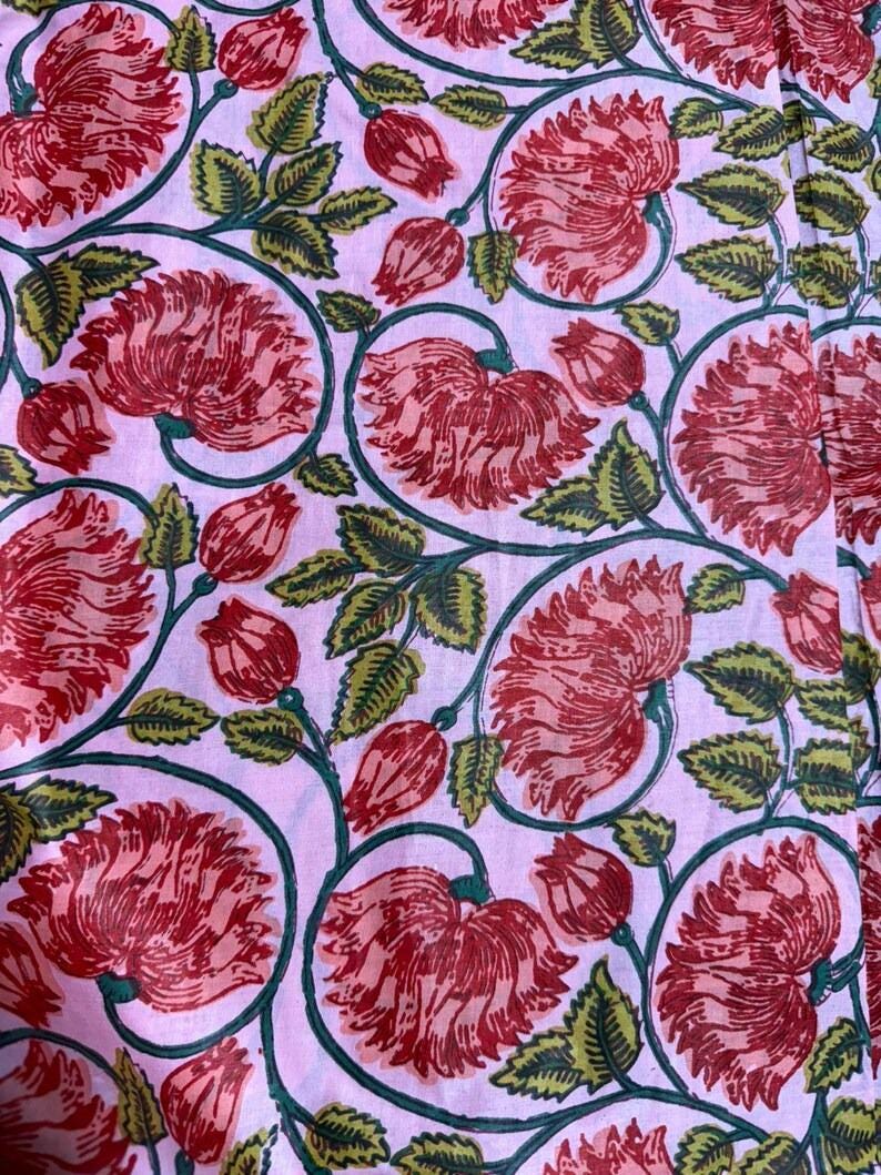 K&ouml;nnte beinhalten: Ein Stoff mit einem sich wiederholenden Blumenmuster. Gro&szlig;e rote Bl&uuml;ten und Knospen vor einem hellrosa Hintergrund, mit gr&uuml;nen Bl&auml;ttern als Kontrast. Die Bl&uuml;ten sind detailliert, und die Bl&auml;tter haben eine strukturierte Optik. Geeignet f&uuml;r Textilien oder Heimtextilien.